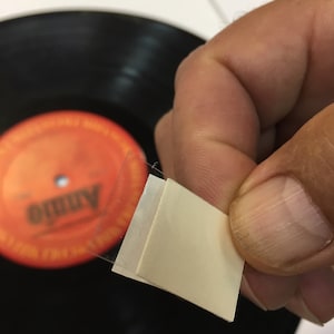 May include: A clear plastic square with a white adhesive backing. The adhesive is used to attach a record to a turntable.