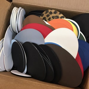May include: A cardboard box filled with a variety of colorful felt circles and ovals. The circles and ovals are in various sizes and colors, including red, blue, green, brown, black, white, and orange.