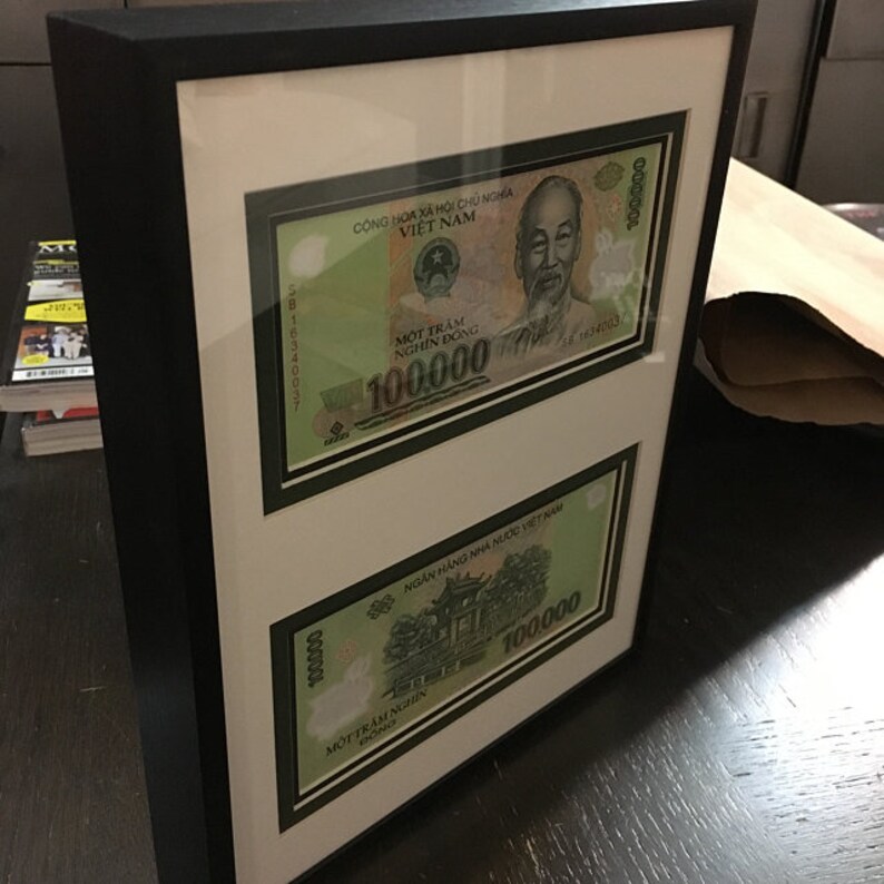 May include: Two framed Vietnamese banknotes, each featuring a portrait of a man and the text "Cộng H&ograve;a X&atilde; Hội Chủ Nghĩa Việt Nam" and "MỘT TR&Aacute;M NGH&Igrave;N ĐỒNG" with the denomination "100.000" printed in green.