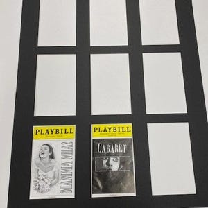 May include: Black picture frame with nine rectangular openings. Two playbills are visible, one for "Mamma Mia!" and one for "Cabaret". The playbills are yellow and white with black text and images. The frame is on a white surface.