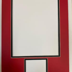 May include: A rectangular red picture frame mat with a large vertical white opening and a smaller horizontal white opening below it. Each opening is bordered by a thin black frame accent, creating a layered appearance for displaying two separate items.