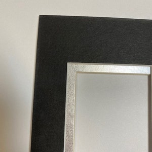 K&ouml;nnte beinhalten: Ein schwarzer Bilderrahmen mit silbernem Rand und wei&szlig;em Innenraum. Der Rahmen dient dazu, ein Foto oder Kunstwerk einzurahmen. Der schwarze Rahmen bietet einen kontrastierenden Rand, w&auml;hrend das Silber einen Hauch von Eleganz verleiht.