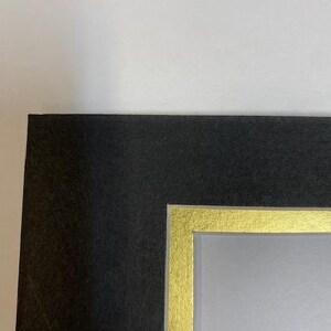 K&ouml;nnte beinhalten: Ein schwarzer Bilderrahmen mit einem goldenen Innenrand. Der Rahmen hat eine strukturierte Oberfl&auml;che und einen wei&szlig;en Hintergrund. Die Ecke des Rahmens ist vor einem wei&szlig;en Hintergrund sichtbar.