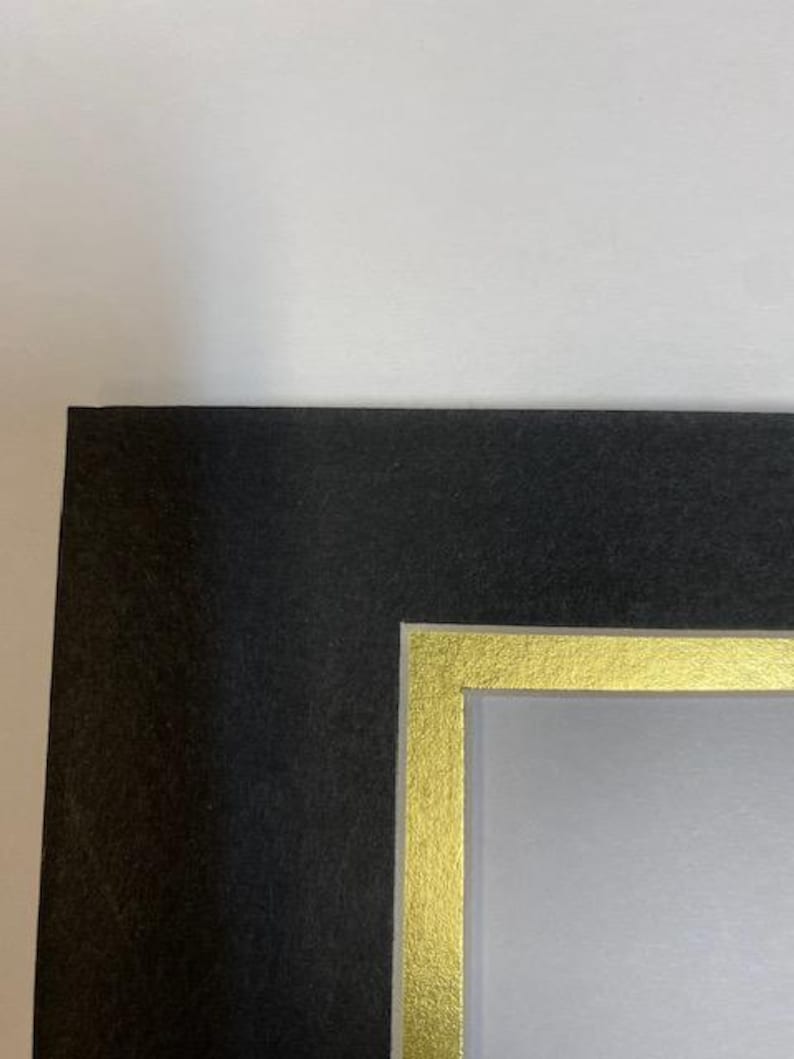 K&ouml;nnte beinhalten: Ein schwarzer Bilderrahmen mit einem goldenen Innenrand. Der Rahmen hat eine strukturierte Oberfl&auml;che und einen wei&szlig;en Hintergrund. Die Ecke des Rahmens ist vor einem wei&szlig;en Hintergrund sichtbar.