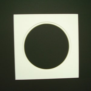 May include: White square picture frame with a circular opening in the center. The frame is made of a smooth, white material.