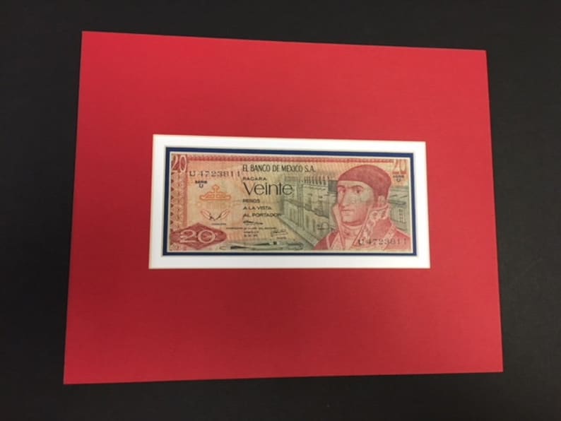 May include: A framed 20 peso bill from the Banco de Mexico, S.A. The bill features a portrait of a man in a military uniform, with the text "Veinte" in red and the words "Banco de Mexico, S.A." in blue.