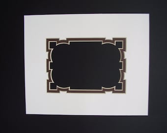 May include: A white mat with a brown and cream colored decorative frame. The frame has a scalloped design.