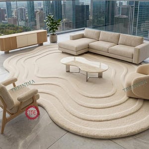 Op de afbeelding: Een moderne woonkameropstelling met een beige hoekbank, een gebogen fauteuil en een houten armstoel. Een uniek, crèmekleurig, golvend vloerkleed vormt de basis van de ruimte, aangevuld met een marmeren salontafel en een houten kast. De kamer kijkt uit op een stadsgezicht.