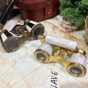 May include: Two pairs of antique opera glasses with brass frames and white and black accents. One pair has a black handle, the other has a white handle. They rest on a map with the word "WAVE" written on it.