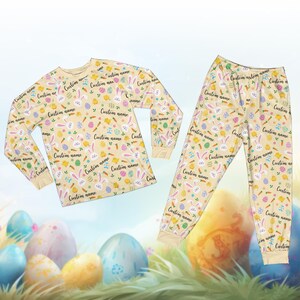 May include: A beige Easter-themed pajama set with a long-sleeved top and pants. The set is covered in a pattern of Easter eggs, bunnies, carrots, and the text "Custom name". The pajamas are designed for comfort and seasonal celebrations.
