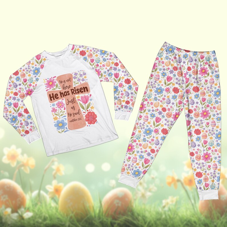 May include: White Easter-themed pajama set. The long-sleeved top features a cross design with the text "He has Risen". The sleeves and pajama pants are covered in a floral and Easter egg pattern. The pajama set is designed for comfort and seasonal celebrations.