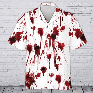 May include: A short-sleeved button-down shirt featuring a white base color with a repeating pattern of dark red blood splatters and dark circular bullet hole graphics distributed across the front, collar, and sleeves of the garment.