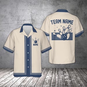 Pode incluir: Camisa de boliche creme com detalhes em azul marinho e um desenho de pinos de boliche. A frente apresenta um desenho de pinos de boliche e a palavra "NAME". A parte de trás exibe "TEAM NAME" acima de um desenho de pinos e bola.