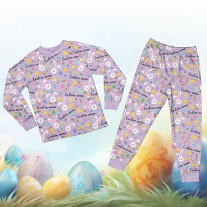 May include: A lilac-colored pajama set featuring a repeating pattern of Easter bunnies, eggs, carrots, and chicks. The long-sleeved top and pants are adorned with the text "Custom name". The set is designed for comfort and festive occasions.