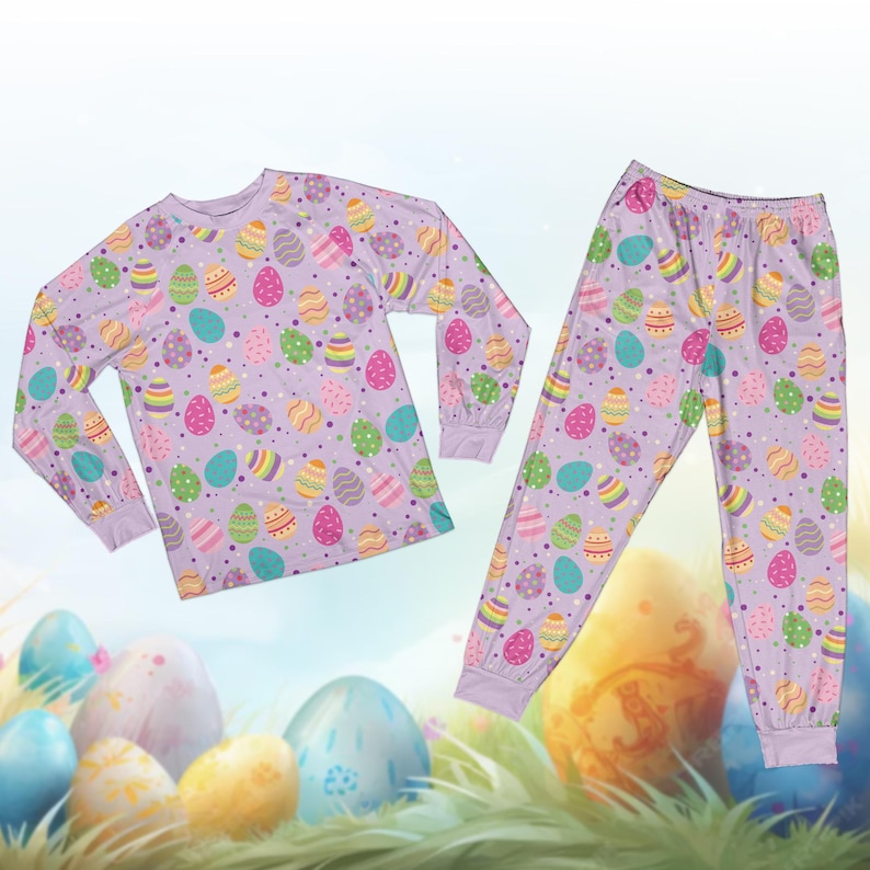May include: A lilac-colored pajama set featuring a long-sleeved top and matching pants. The set is covered in a pattern of colorful Easter eggs in various designs and colors, including yellow, pink, blue, and green. The pajamas have a comfortable, relaxed fit.
