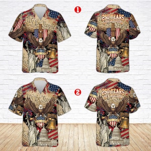 K&ouml;nnte beinhalten: Kurz&auml;rmelige Hemden mit Knopfleiste und patriotischen Designs. Die Hemden zeigen einen Adler, die Freiheitsglocke, die Freiheitsstatue und das US-Kapitol mit dem Text "We the People" und "250 Years of Freedom".
