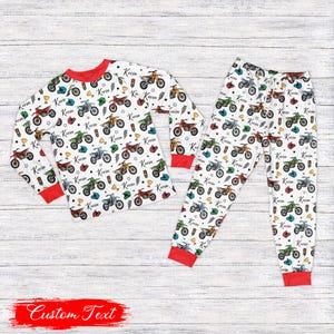 Op de afbeelding: Witte pyjamaset met een motorpatroon. De top met lange mouwen en de broek hebben een herhalend ontwerp van kleurrijke motorfietsen, helmen en sterren. De manchetten en de halslijn zijn rood. De naam "Kevin" staat afgedrukt. De onderkant van de afbeelding heeft de tekst "Custom Text".