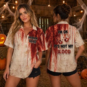 Peut inclure: Une chemise à manches courtes boutonnée avec une base beige et un motif d'éclaboussures de sang rouge. Le devant porte le texte "PROBLEM SOLVED" et le dos affiche deux empreintes de mains avec le texte "I'M OK IT'S NOT MY BLOOD" en police usée.