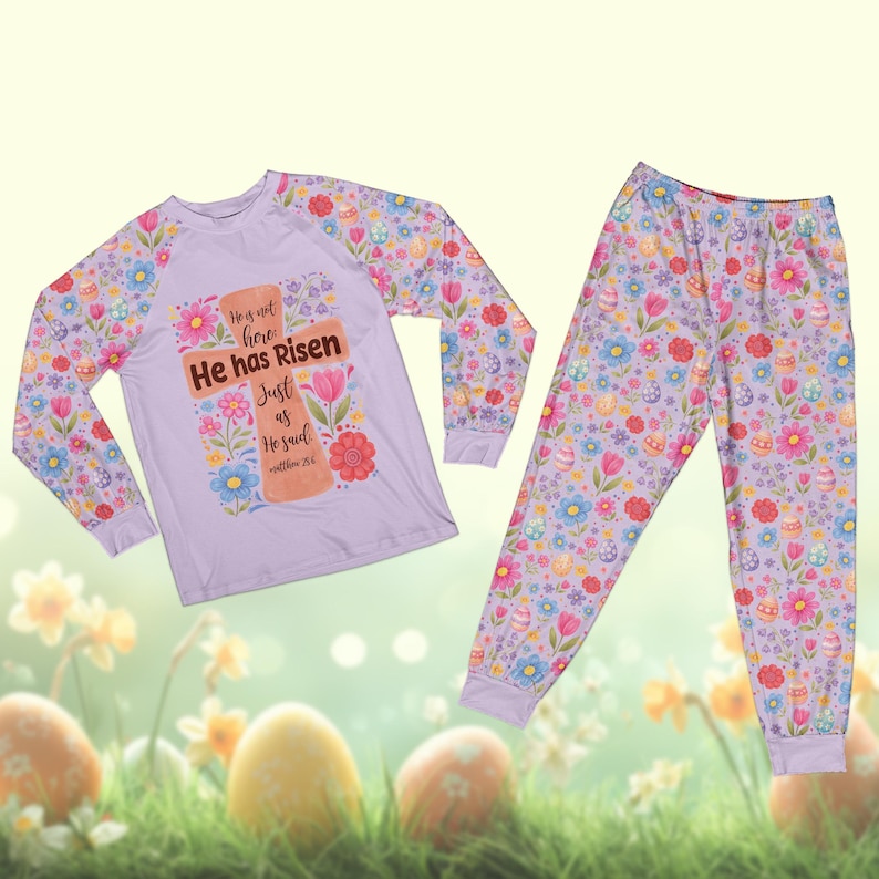May include: A light purple pajama set featuring a long-sleeved shirt and pants. The shirt has a cross design with the text "He has Risen". The set is decorated with floral and Easter egg patterns.