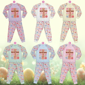 May include: Six sets of children's pajamas with long sleeves and pants. Each set features a floral pattern on the pants and sleeves, and a central graphic with the text "He has Risen". The tops are in various pastel colors, including lavender, white, yellow, mint, blue, and pink.