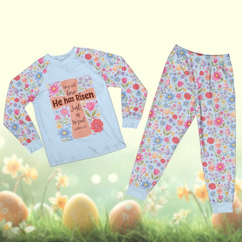 May include: A light blue pajama set with a floral and Easter egg pattern. The long-sleeved top features a cross design with the text "He has Risen". The matching pants have a similar floral and egg design.