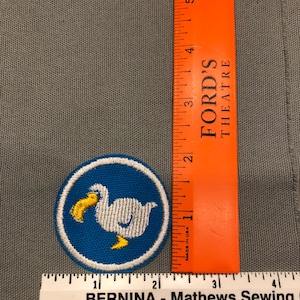 Op de afbeelding: Een witte geborduurde patch met een blauwe achtergrond en een witte vogel met een gele snavel en poten. De patch is rond en heeft een witte rand. De patch is ongeveer 5 cm in diameter.