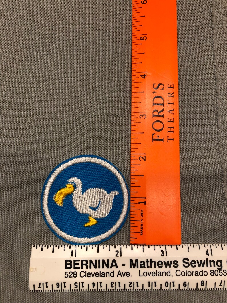 Op de afbeelding: Een witte geborduurde patch met een blauwe achtergrond en een witte vogel met een gele snavel en poten. De patch is rond en heeft een witte rand. De patch is ongeveer 5 cm in diameter.