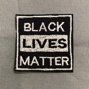 May include: Black Lives Matter patch with white lettering on a black background. The patch is surrounded by a white border.