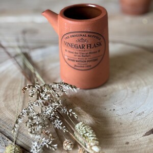 May include: A white ceramic mug with a black handle and the text "But First, Coffee" in a bold, black font. The mug is set against a blurred background, suggesting a cosy setting.