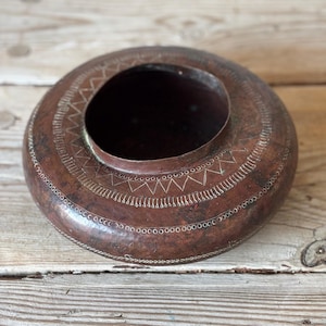 May include: A circular copper bowl with a wide rim and a central opening. The rim is adorned with a repeating pattern of small triangles and dots. The bowl has a dark, aged patina, indicating it is vintage. The diameter is approximately 25 cm.