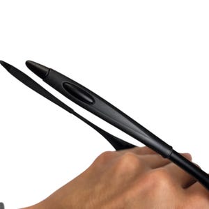 May include: Black eyeglasses arm with a curved design. The arm is held in a hand against a white background. The arm has a rounded tip and a groove along its length.