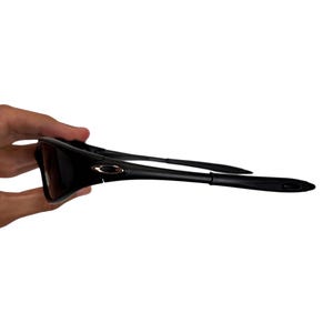 May include: Black sunglasses with a sleek, modern design. The sunglasses have dark lenses and a black frame. The arms of the sunglasses are thin and curve slightly. The Oakley logo is visible on the frame.