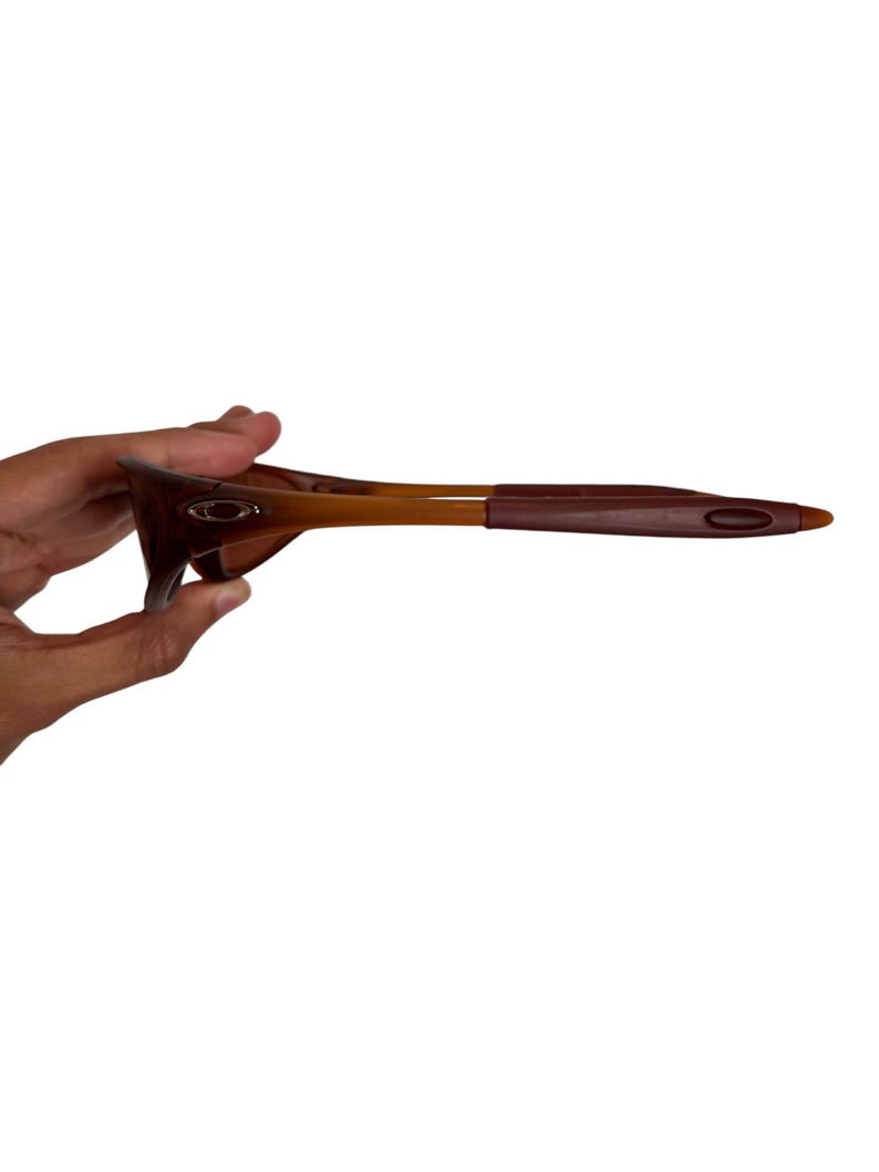 May include: Brown and tan sunglasses with a curved frame and dark brown arms. The sunglasses have a sleek, modern design, suitable for outdoor activities. The lenses are not visible in this image.