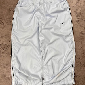 Puede incluir: Pantalones deportivos de color azul claro con cintura elástica y un logotipo Nike swoosh negro en el muslo izquierdo. Los pantalones cuentan con una fina raya vertical negra a lo largo de cada pierna y puños elásticos en el dobladillo.