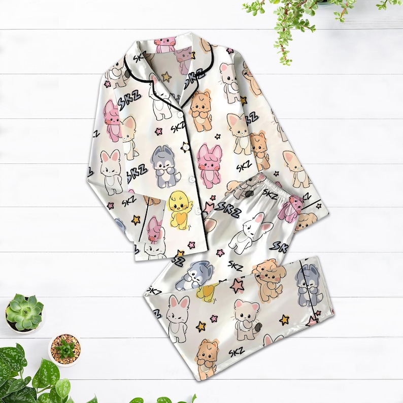 May include: White satin pajama set with a repeating pattern of cartoon animals and stars. The set includes a button-down top with black trim and matching pants. The text "SKZ" is printed throughout the design.
