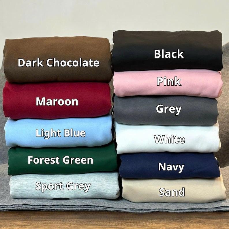 May include: A stack of folded fabric in various colors, including dark chocolate, maroon, light blue, forest green, and sport grey. The stack also includes black, pink, grey, white, navy, and sand-colored fabrics. Each color is labeled with its name in white text.