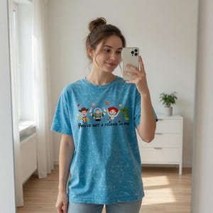 Puede incluir: Camiseta azul claro con efecto tie-dye, con la frase "You've got a friend in me" y personajes de dibujos animados. La camiseta tiene mangas cortas y cuello redondo.