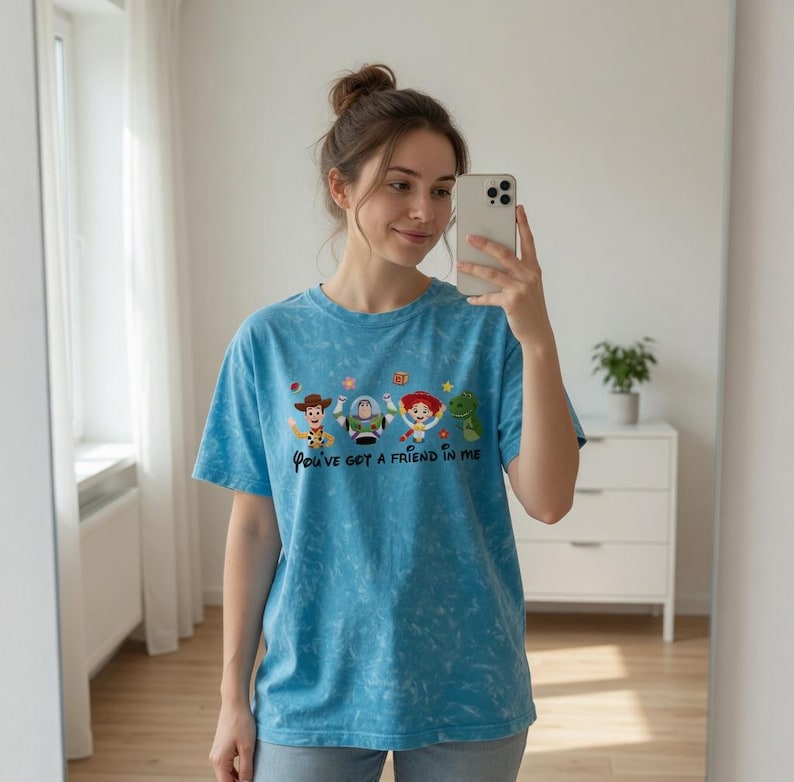 Puede incluir: Camiseta azul claro con efecto tie-dye, con la frase "You've got a friend in me" y personajes de dibujos animados. La camiseta tiene mangas cortas y cuello redondo.