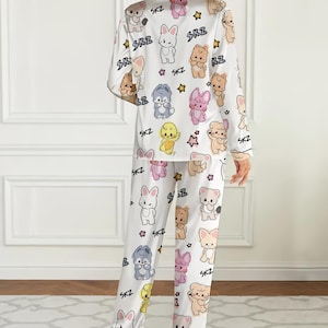 May include: White pajama set featuring a repeating pattern of cartoon animals, stars, and the letters "SKZ". The long-sleeved top and pants are made of a soft material. The pajama set is designed for comfort and relaxation.