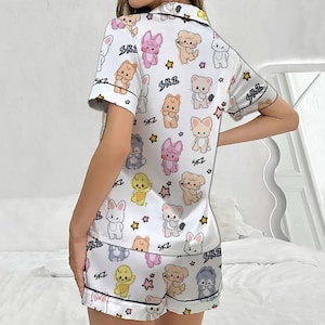 May include: White satin pajama set with a repeating pattern of cartoon animals and stars. The short-sleeved top and shorts are trimmed with black piping and feature the text "SKZ".