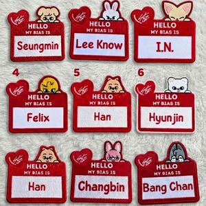 May include: A collection of nine red name tag patches with various cartoon animal designs. Each patch has the text "HELLO MY BIAS IS" and a name, including Seungmin, Lee Know, I.N., Felix, Han, Hyunjin, Changbin, and Bang Chan.