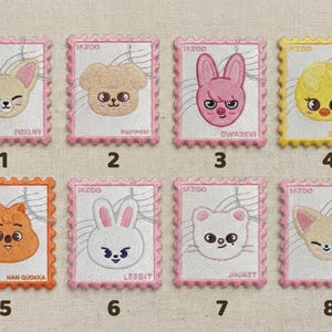 Peut inclure: Écussons brodés en forme de timbres-poste, chacun représentant un visage d'animal de dessin animé. Les écussons sont de différentes couleurs, dont le rose, l'orange et le jaune, avec le texte "SKZOO" et les noms des personnages.