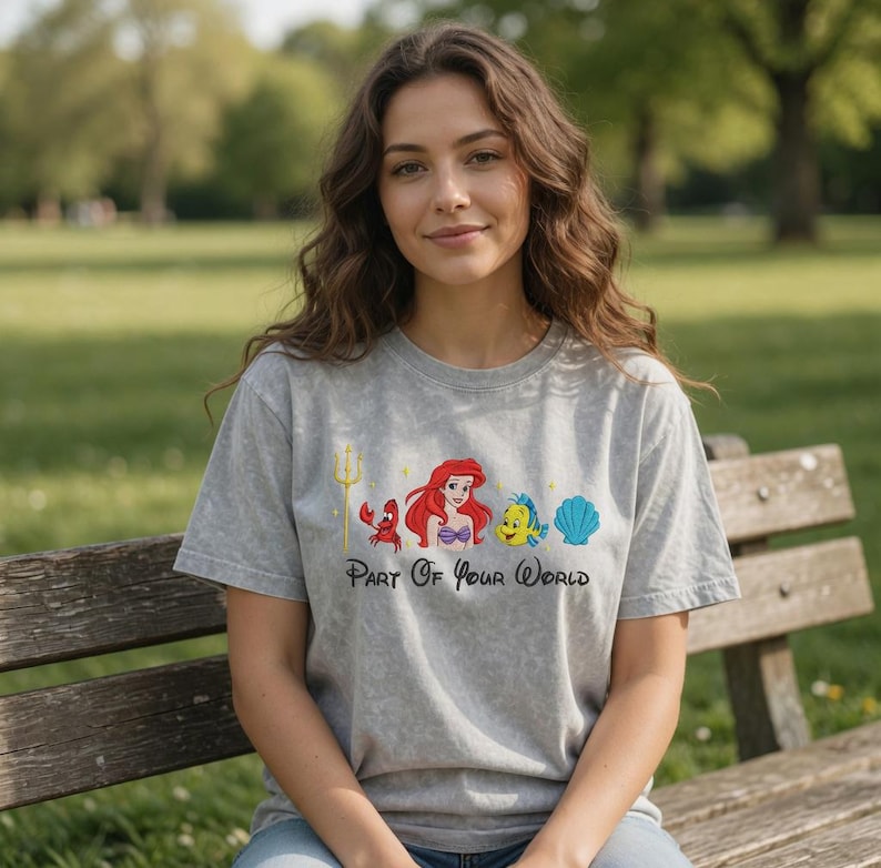 Puede incluir: Una camiseta gris con un gr&aacute;fico colorido de personajes de una popular pel&iacute;cula animada. El dise&ntilde;o incluye un tridente, un cangrejo, una sirena, un pez y una concha, con el texto "Part Of Your World" debajo. La camiseta es de material suave.