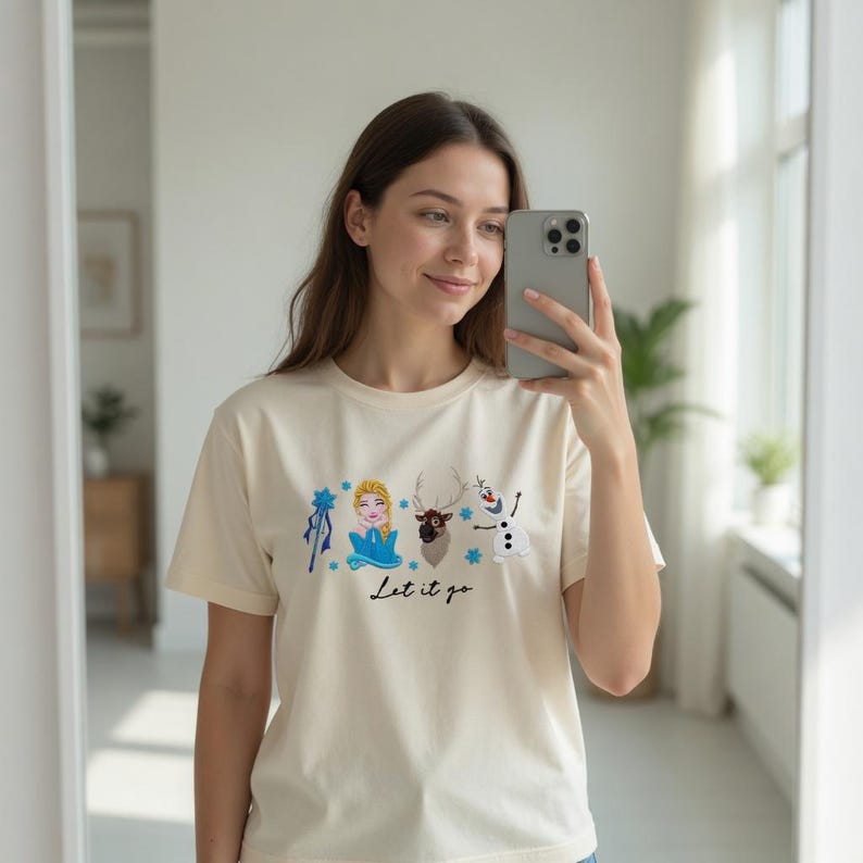 Puede incluir: Camiseta color crema con un gr&aacute;fico de personajes de la pel&iacute;cula Frozen, incluyendo a Elsa, un reno y Olaf el mu&ntilde;eco de nieve. La frase "Let it go" est&aacute; escrita en gui&oacute;n negro debajo. La camiseta tiene mangas cortas.