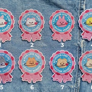 May include: Eight pink and blue embroidered patches with cartoon animal designs. Each patch features a different animal, the text "LOVE CLUB", and "LIFETIME MEMBER". The patches are on a denim background.