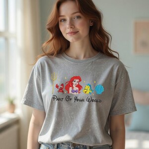 Puede incluir: Camiseta gris con un gr&aacute;fico colorido de Ariel, Flounder, Sebasti&aacute;n y una concha. El texto "Part Of Your World" est&aacute; impreso debajo de los personajes. La camiseta tiene mangas cortas y cuello redondo.