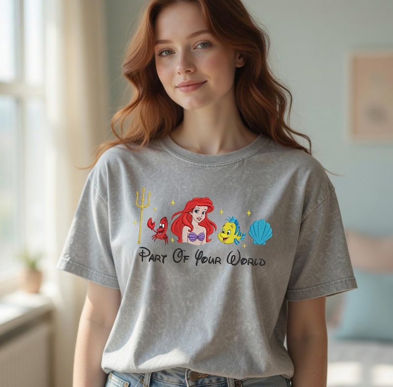 Puede incluir: Camiseta gris con un gr&aacute;fico colorido de Ariel, Flounder, Sebasti&aacute;n y una concha. El texto "Part Of Your World" est&aacute; impreso debajo de los personajes. La camiseta tiene mangas cortas y cuello redondo.