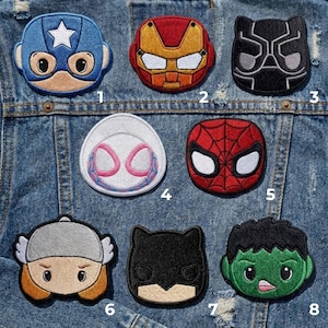 Puede incluir: Ocho parches bordados con superhéroes, incluyendo Capitán América, Iron Man, Pantera Negra, Spider-Man, Spider-Gwen, Thor, Batman y Hulk. Los parches son de varios colores y diseños, y están adheridos a una chaqueta vaquera.