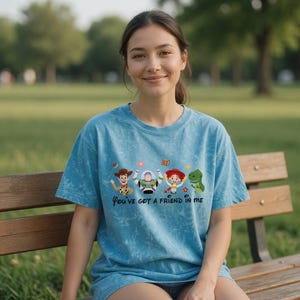 Puede incluir: Una camiseta azul te&ntilde;ida con la frase "You've got a friend in me" y personajes de dibujos animados. Los personajes incluyen un vaquero, un guardabosques espacial, una vaquera y un dinosaurio verde. La camiseta la lleva una persona.