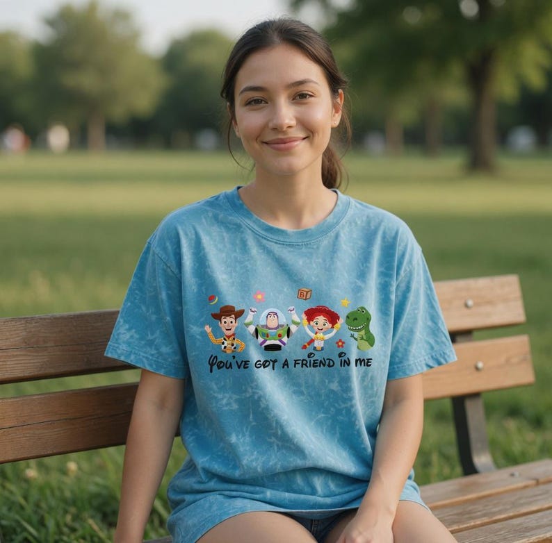 Puede incluir: Una camiseta azul te&ntilde;ida con la frase "You've got a friend in me" y personajes de dibujos animados. Los personajes incluyen un vaquero, un guardabosques espacial, una vaquera y un dinosaurio verde. La camiseta la lleva una persona.